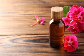 Geranium essential oil in bottle and beautiful flowers on wooden table, space for text