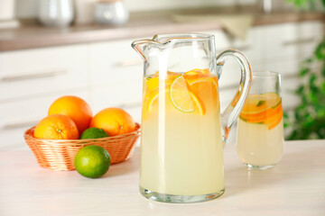 Refreshing lemonade with orange and lime in jug on white wooden table