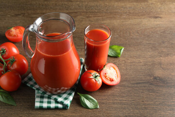 Tasty tomato juice in jug, glass and vegetables on wooden table. Space for text