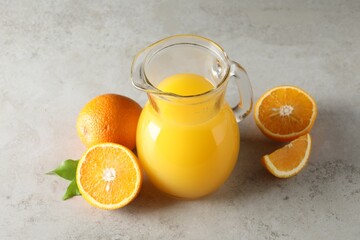Tasty orange juice in jug and citrus fruits on light textured table