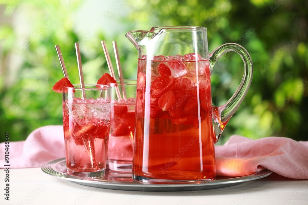 Wall mural Tasty strawberry lemonade in jug and glasses on white table against blurred green background