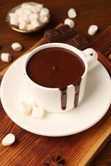 Tasty melted chocolate in cup and marshmallows on wooden table