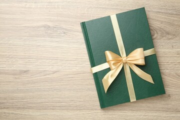 Book tied with golden ribbon on wooden table, top view. Space for text