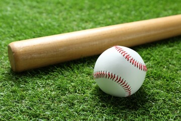 Baseball ball and bat on green grass outdoors, closeup