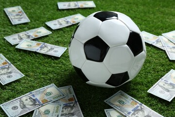 Soccer ball and dollar banknotes on green grass outdoors