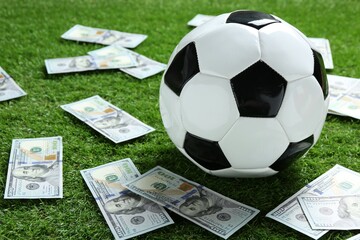 Soccer ball and dollar banknotes on green grass outdoors