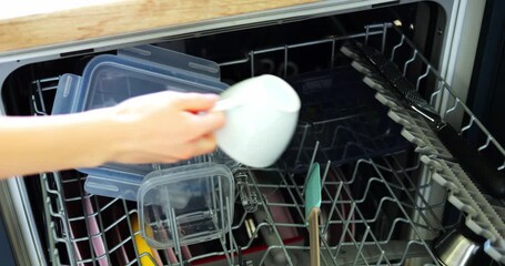 Maid hand takes washed coffee cup out of dishwasher drawer at home closeup. Woman unloads modern kitchen device from dishware. Chores routine