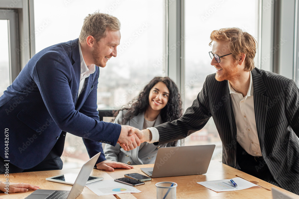 Aufkleber two businessmen in suits are shaking hands in an office setting. they are both smiling and appear to