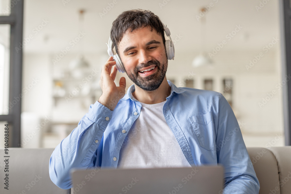 Poster a man wearing headphones sits on a couch in his home, smiling while listening to music. he is workin