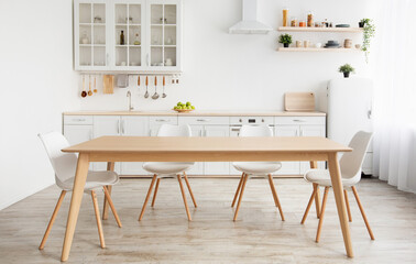 Scandinavian classic white kitchen with wooden details, minimalistic interior design. Modern furniture with accessories and various utensils, table and chairs in dinning room, copy space