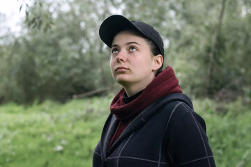 A beautiful girl in a cap and a hoodie looks up in nature