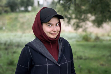A funny girl in a cap and hood with smile in nature