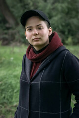 A cute girl in a cap and a hoodie is looking at the camera in nature