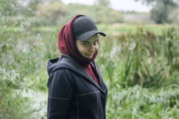 A cute girl in a cap and hood with a smile in nature