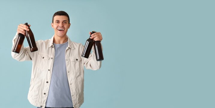 Handsome young man holding bottles of beer on light blue background with space for text - Powered by Adobe