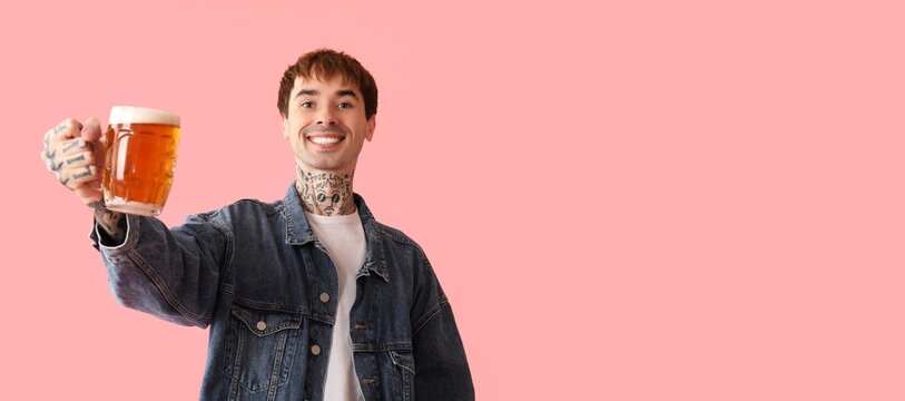 Young tattooed man holding mug of beer on pink background with space for text