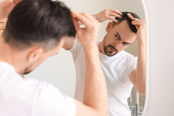 Handsome man combing hair near mirror at home