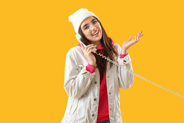 Pretty young woman talking by telephone on yellow background
