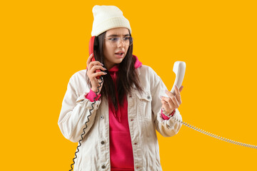 Displeased young woman with telephone receivers on yellow background