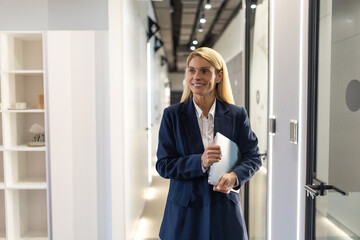 Fototapeta premium Wxecutive businesswoman in official style suit standing in office corridor with laptop in hands