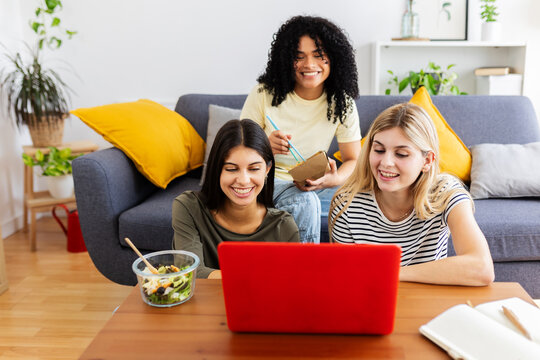 Three happy college female students working together on laptop at home. Education and technology concept.
