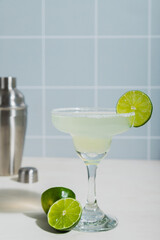 classic margarita cocktail with lime. Checkered tile background. Cocktail silver shaker in the background.