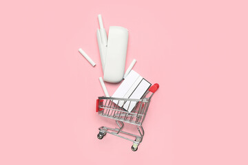 Composition with shopping cart, modern electronic cigar and pack of sticks on pink background