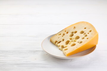 Piece of Emmental cheese with holes on a white plate standibg on a white wooden table