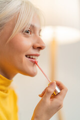 Young woman applying lip gloss smiling in bathroom