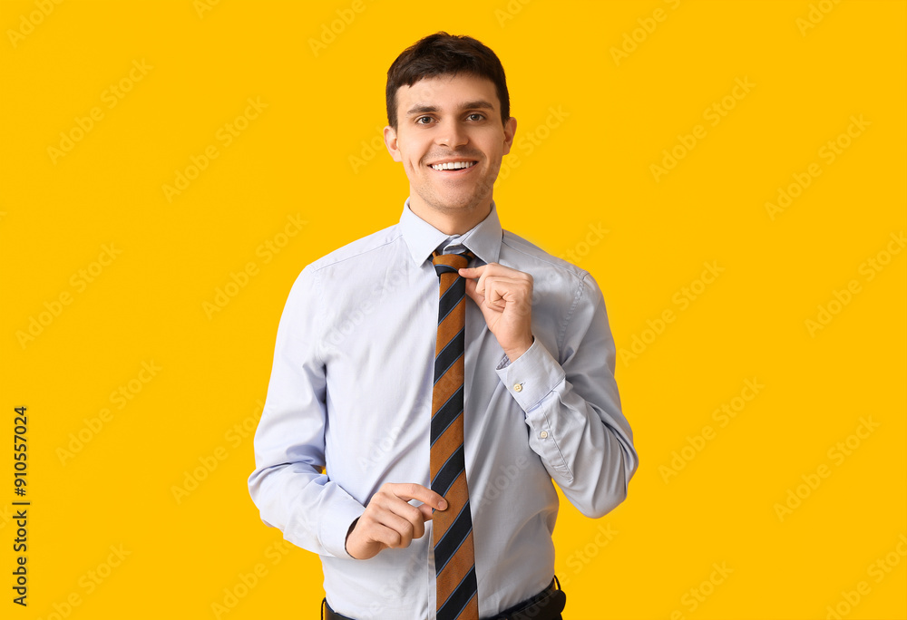 Poster Smiling young man straightening his tie on yellow background