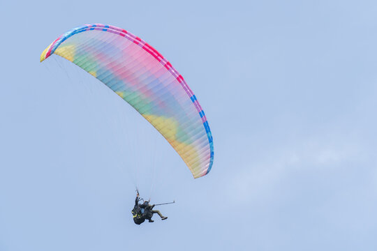 A rainbow-colored paraglider flies in the sky