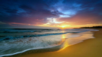 Fototapeta premium High-angle of pristine beach at sunset gentle waves of blue water washing against the golden sand sky tinted in vibrant hues of orange, pink, and purple