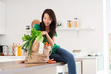 Young Asian woman with bag full of products in kitchen