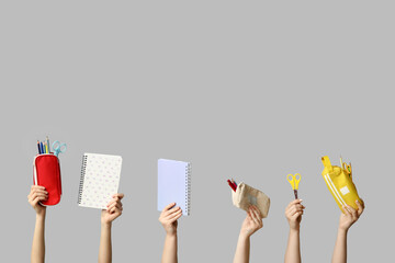 Female hands holding notebooks and pencil cases with stationery on grey background