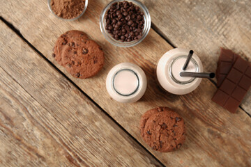 Bottles of sweet chocolate milk with tasty cookies and glass bowl of cocoa powder on wooden background