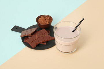 Glass of sweet chocolate milk and bowl with cocoa powder on colorful background