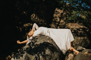 A woman dressed in white rests on rocks in a natural setting, embodying tranquility and relaxation in the outdoors.