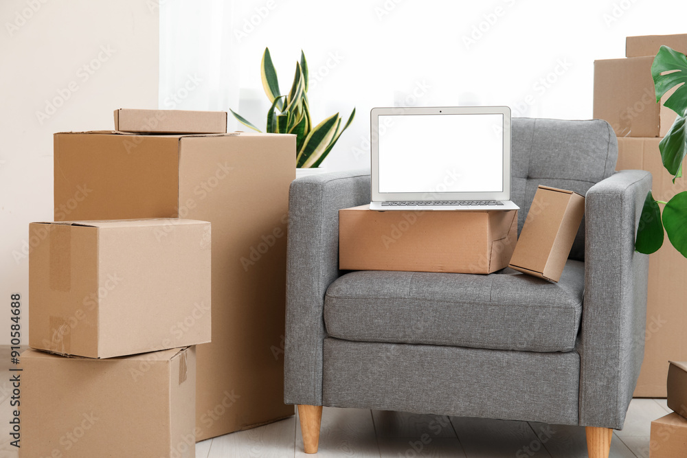 Wall mural Blank laptop with moving boxes on armchair and plants near window in room