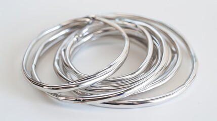 Fototapeta premium Several silver bracelets lay on a white surface, forming a complex and interconnected design