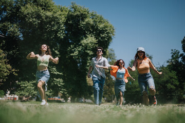 Fototapeta premium Four young friends having fun, running and enjoying a sunny day in the park. Happiness, joy, and friendship capture the carefree spirit of youth.