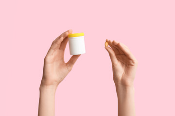 Female hands with pill and pill box on pink background