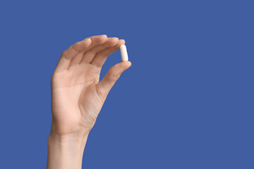 Female hand holding pill on blue background