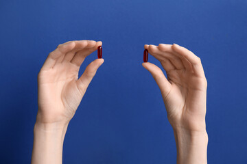 Female hands with red pills on blue background