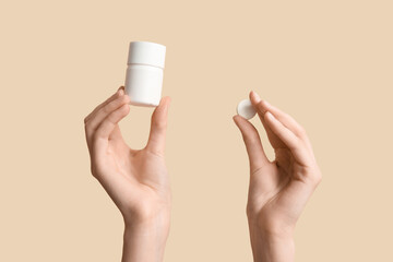 Female hands with pill and pill box on beige background