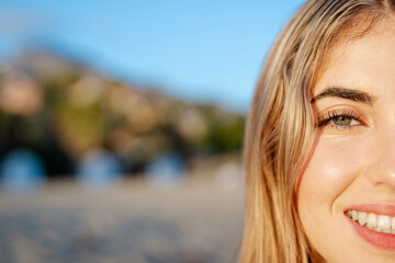 Portrait of one happy young beautiful woman smiling looking at the camera with big blue and green eyes. Female girl at the beach close up face.