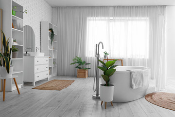 Bathtub, towel and houseplants in interior of light bathroom