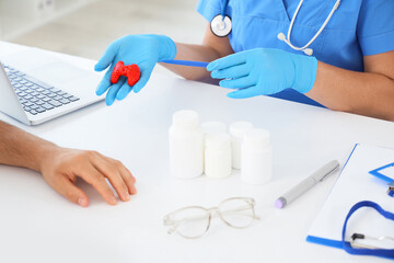 Female endocrinologist showing thyroid gland model to man in clinic, closeup