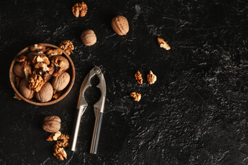 Wooden bowl with tasty walnuts and nutcracker on black background