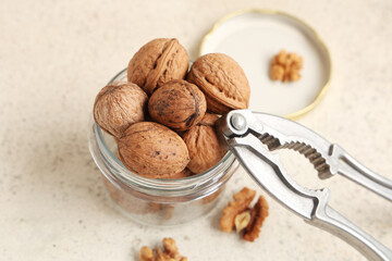 Jar with tasty walnuts and nutcracker on white background