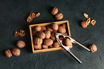 Wooden box with tasty walnuts and nutcracker on dark background